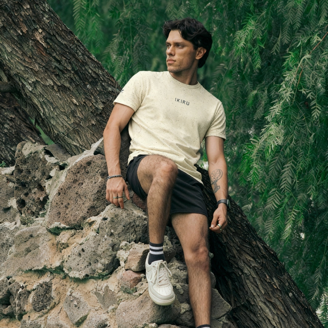 Man wearing a beige IKIRU branded t-shirt sitting on a stone in the forest