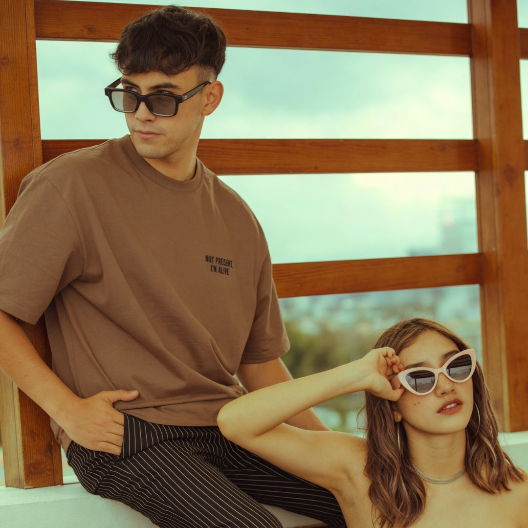 Man and woman sitting down wearing sunglasses and relaxing in the sun wearing IKIRU branded shirts