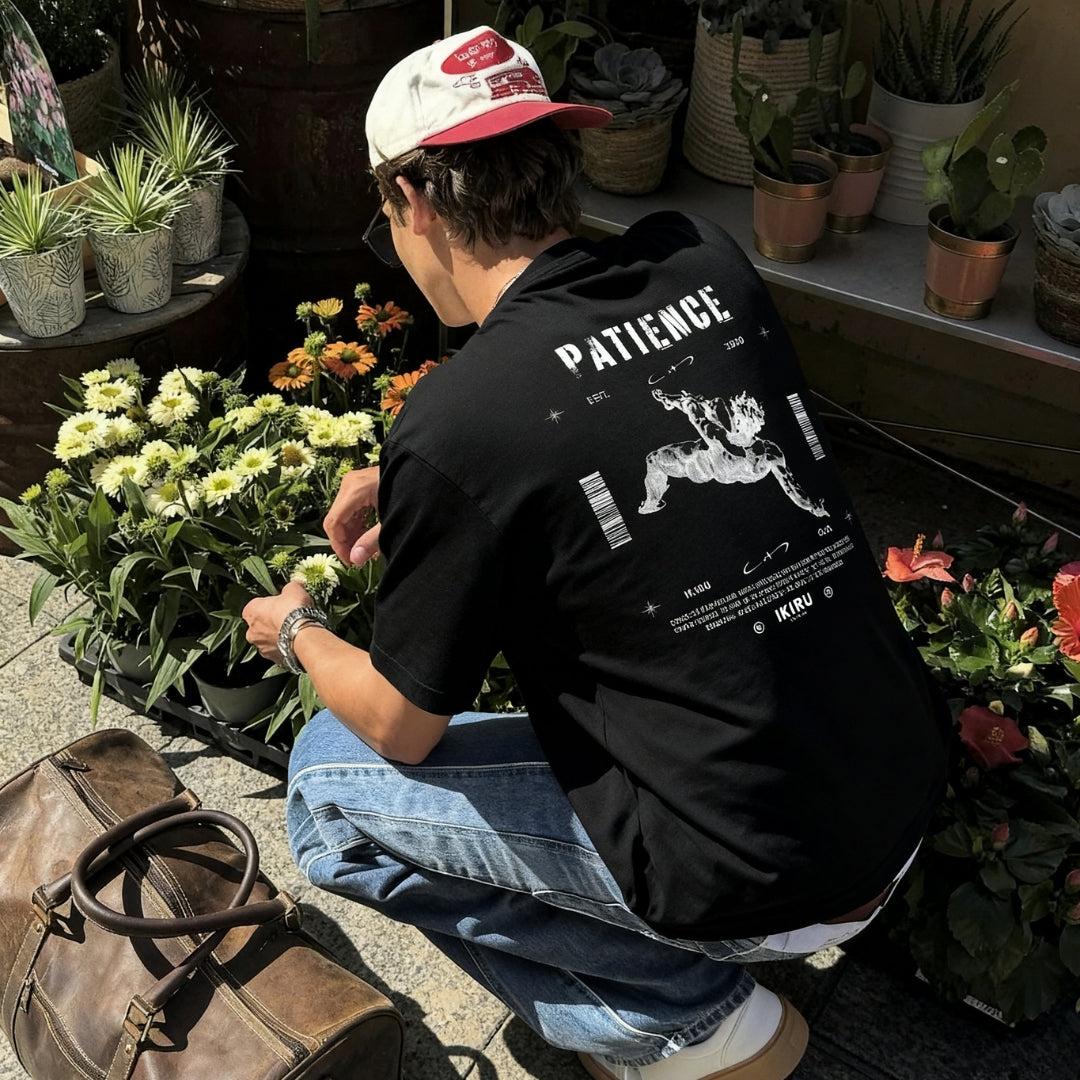 Man sitting down in a garden wearing a black IKIRU branded t-shirt showcasing the backdesign