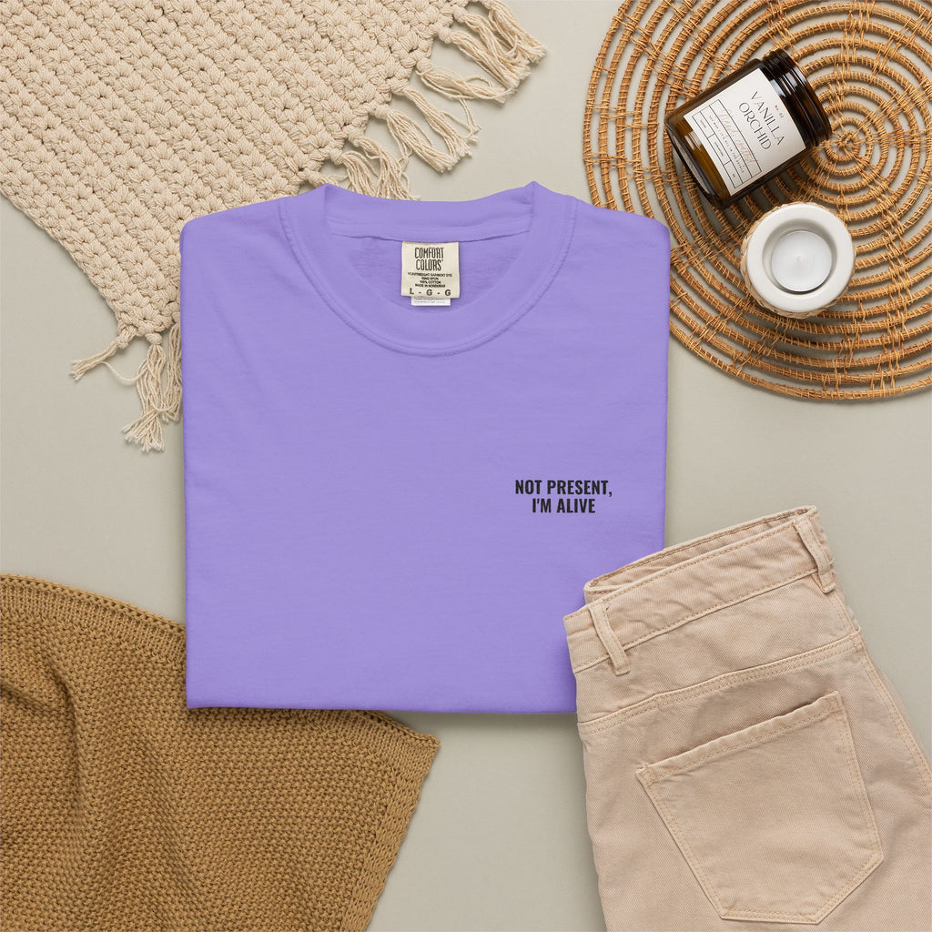 Folded purple t-shirt with text on a neutral surface with accessories.