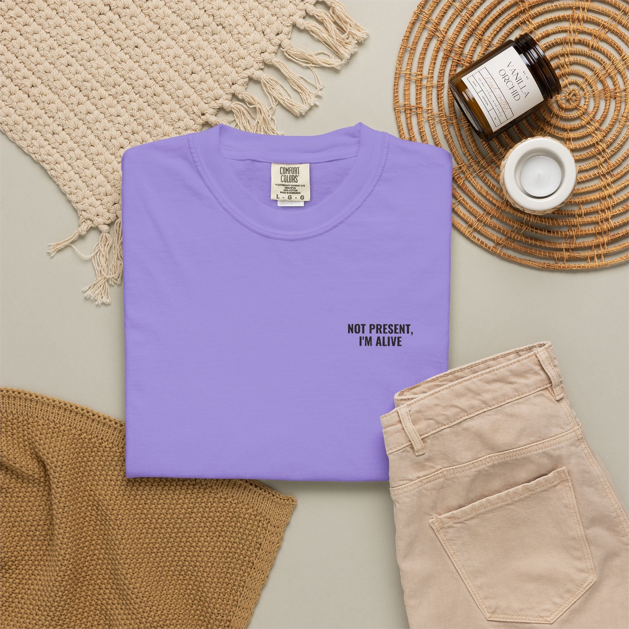 Folded purple t-shirt with text on a neutral surface with accessories.