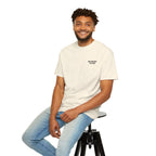 Man sitting on a stool wearing a beige t-shirt and light blue jeans against a white background