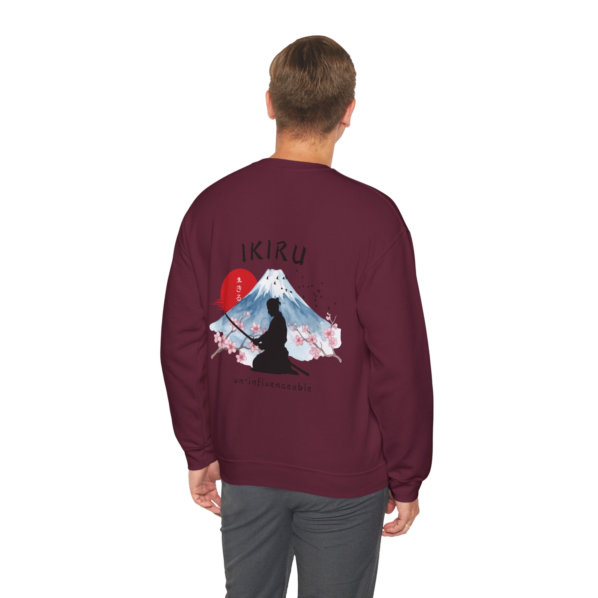 Man wearing maroon sweater with a mountain, samurai, and blossom tree design on the back saying 'un-influenceable' against a white background