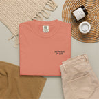 Folded pink t-shirt with 'Not present, I'm alive' label on a neutral background with beige pants and decorative items.