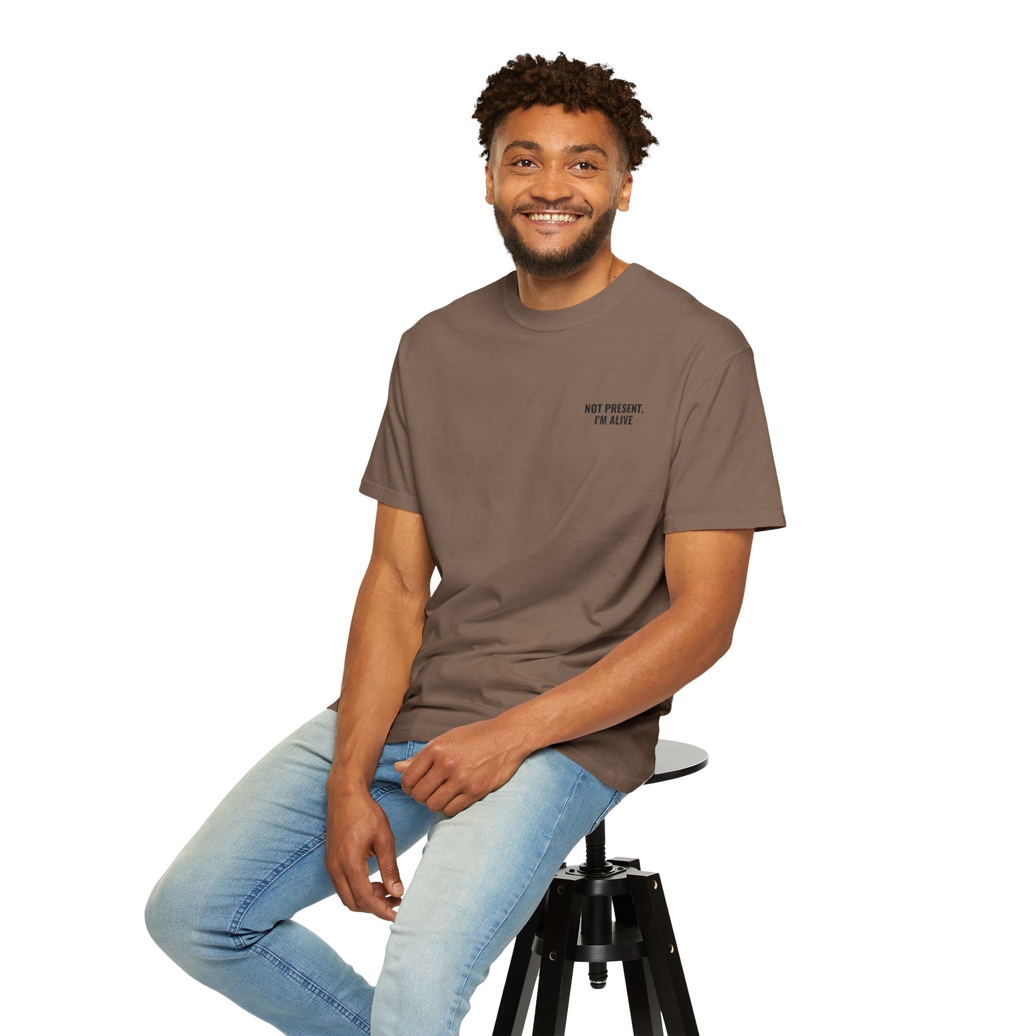 Man sitting on a stool wearing a brown t-shirt with text and light blue jeans on a white background