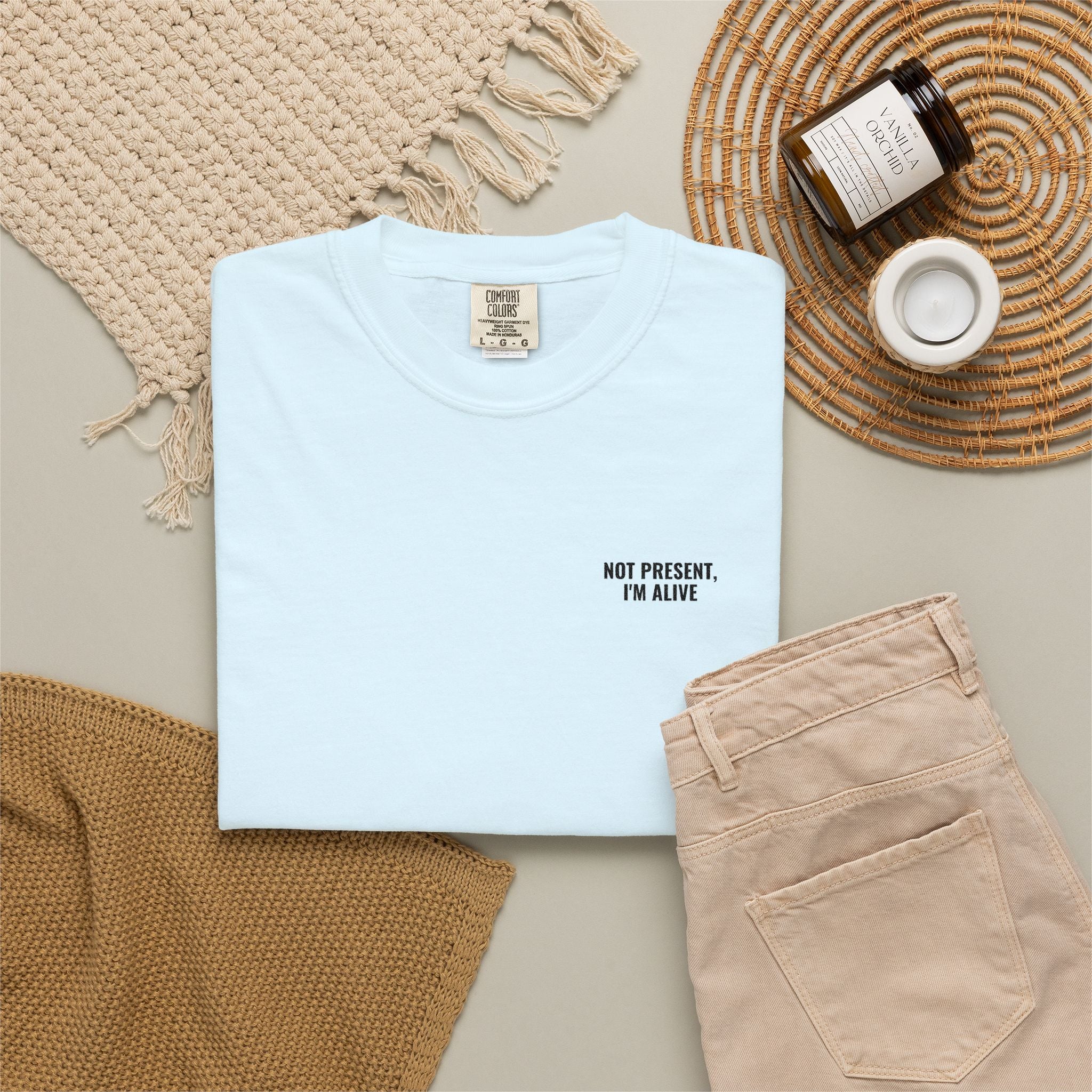 Light blue t-shirt with text, beige pants, and decorative items on a neutral background