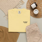 Yellow t-shirt with a design on a gray surface with beige pants and a woven mat.