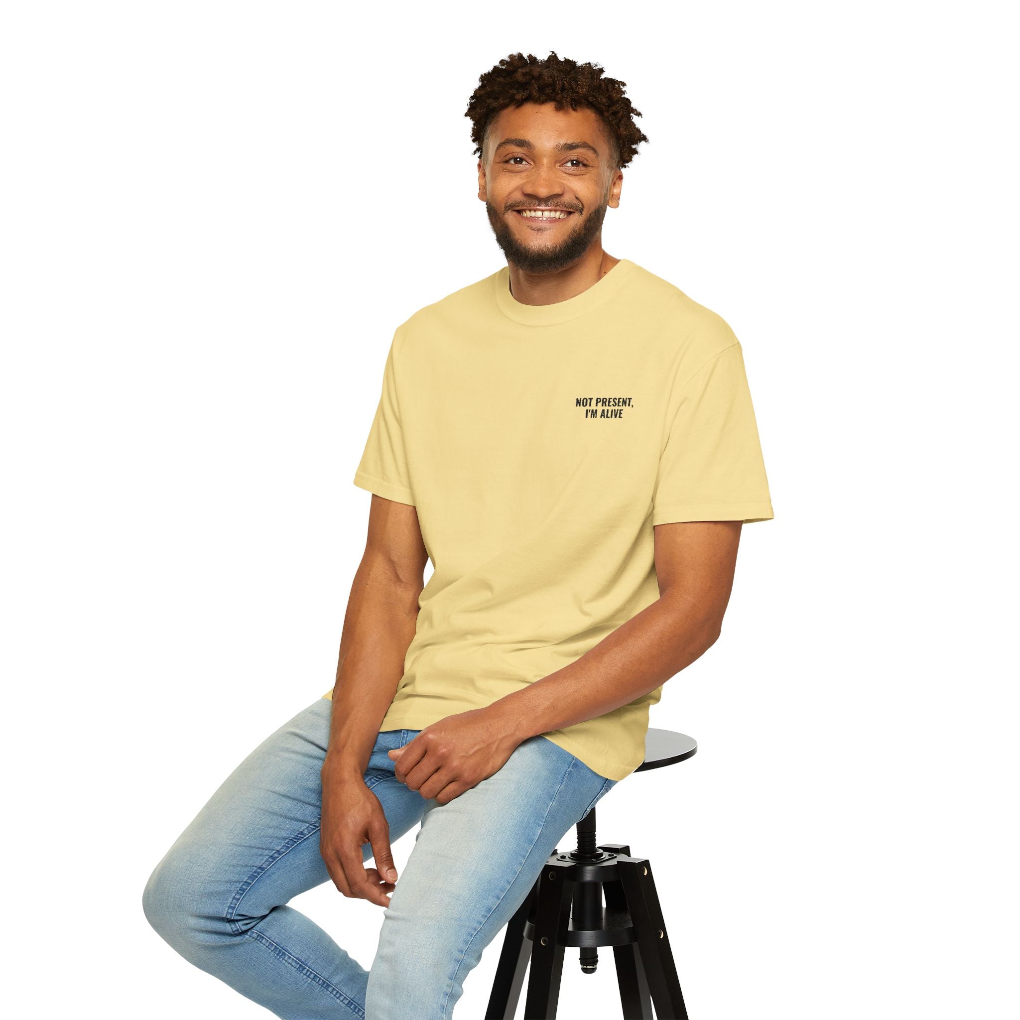 Man sitting on a stool wearing a yellow t-shirt and light blue jeans against a white background