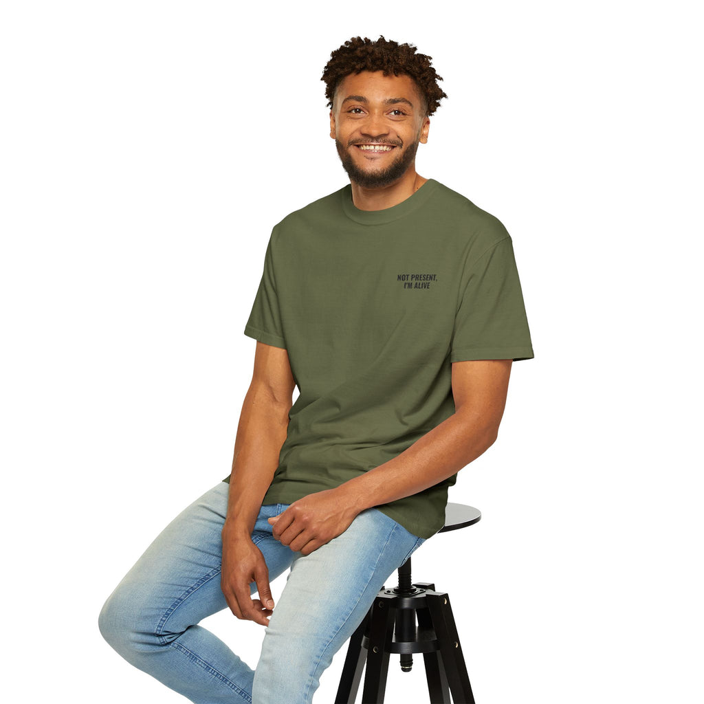 Man sitting on a stool wearing a green t-shirt and light blue jeans against a white background