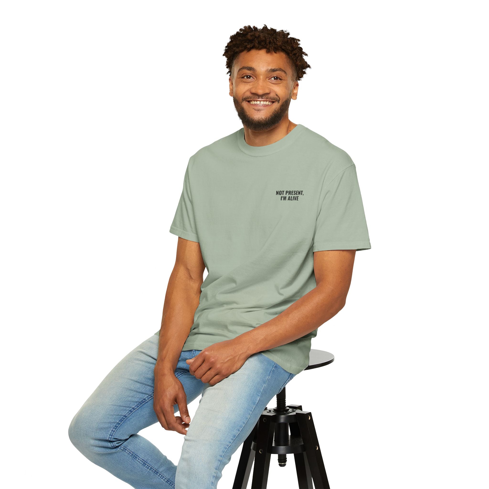 Man wearing a light green t-shirt with a graphic design, sitting on a stool against a white background