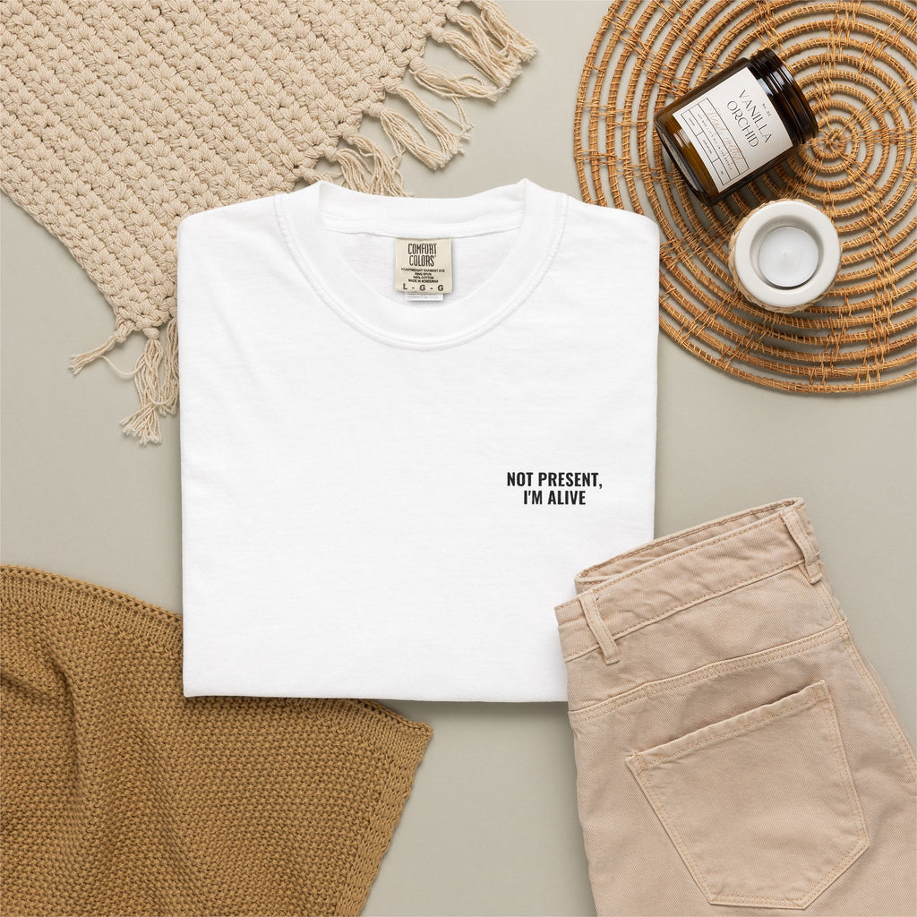 White t-shirt with text, beige pants, and decorative items on a neutral background
