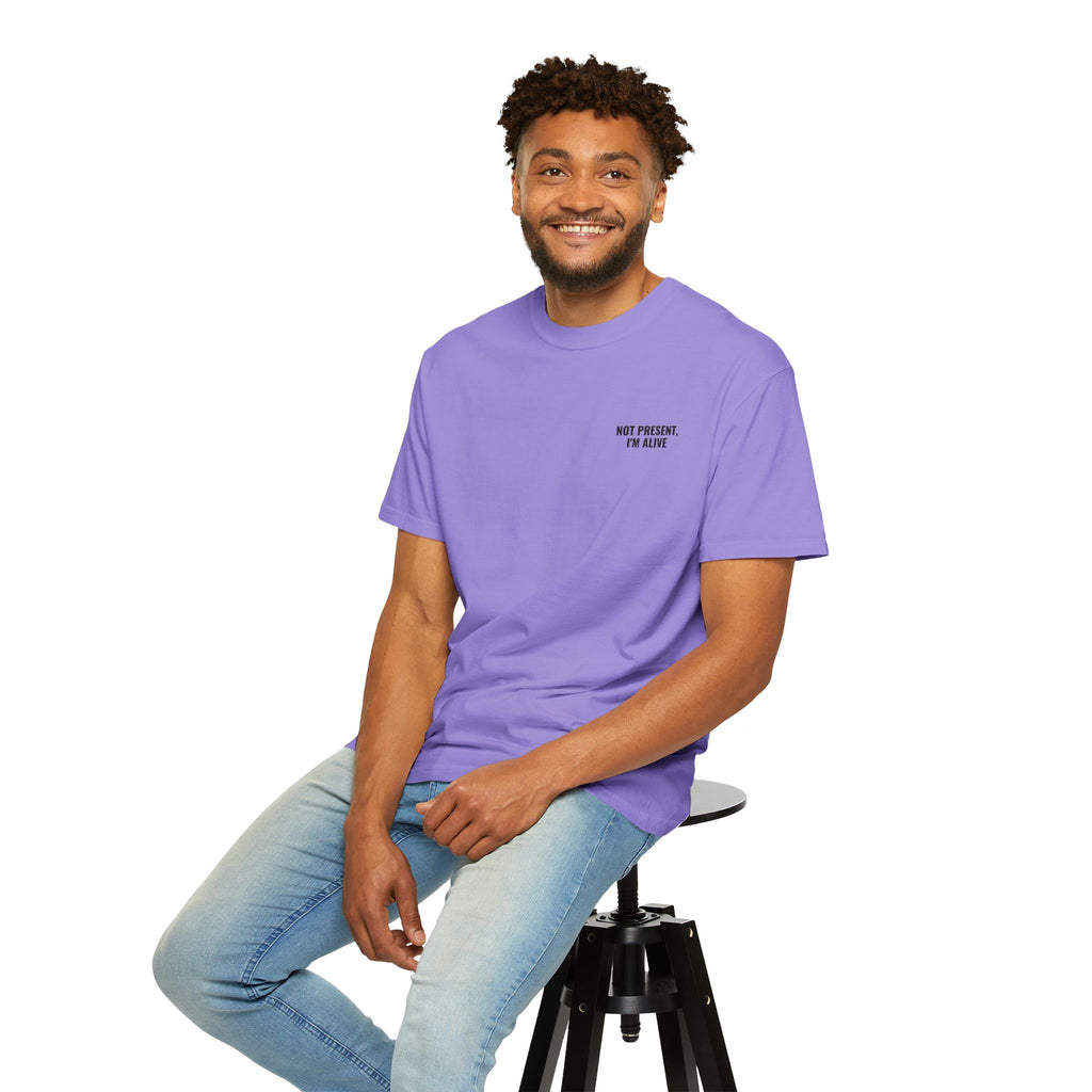 Man wearing a purple t-shirt with 'Not present, I'm alive' and a gold lock design, sitting on a stool.