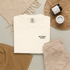 White t-shirt with 'Not present, I'm alive' text, beige pants, and a bottle on a textured surface.