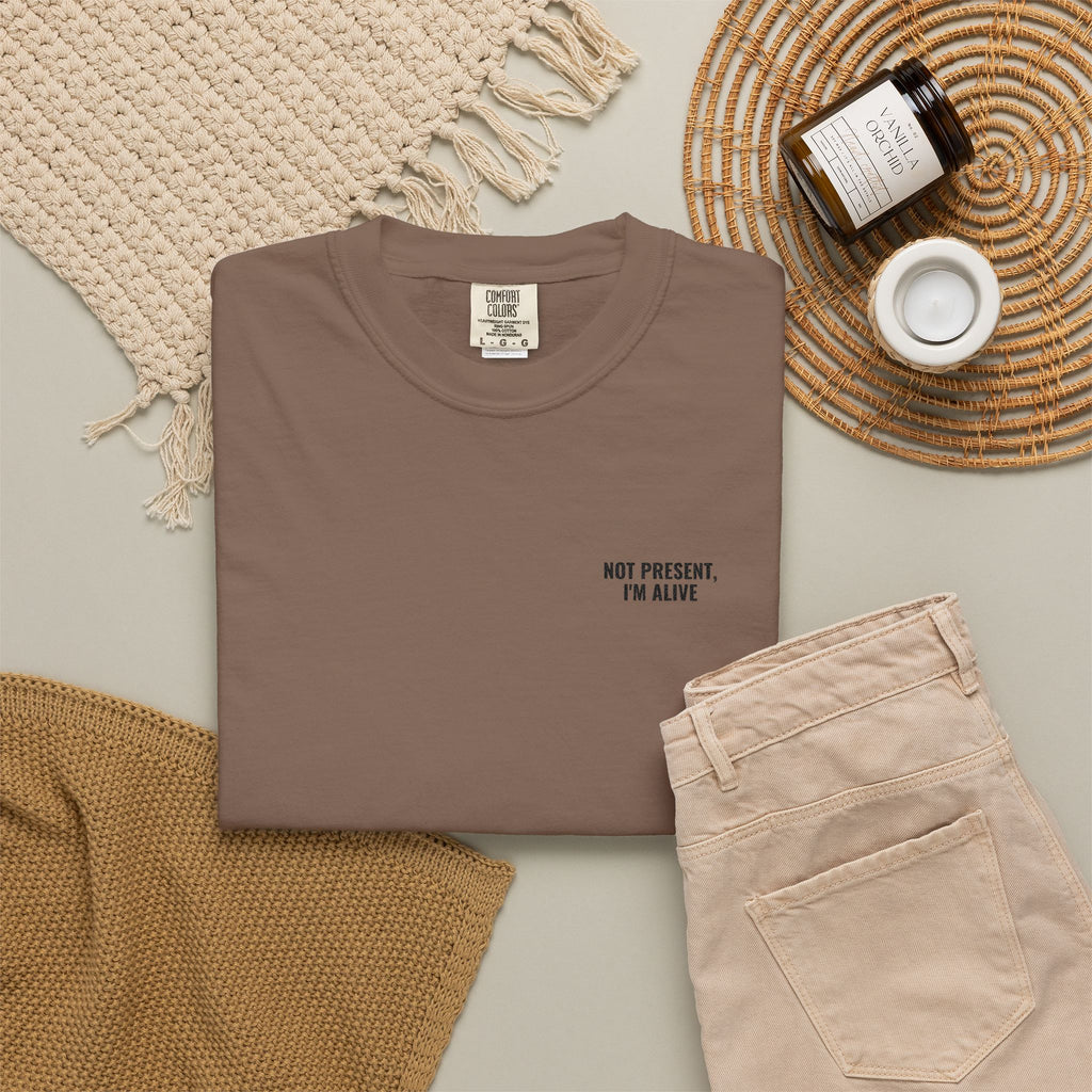 Folded brown t-shirt with text on a neutral surface with accessories.