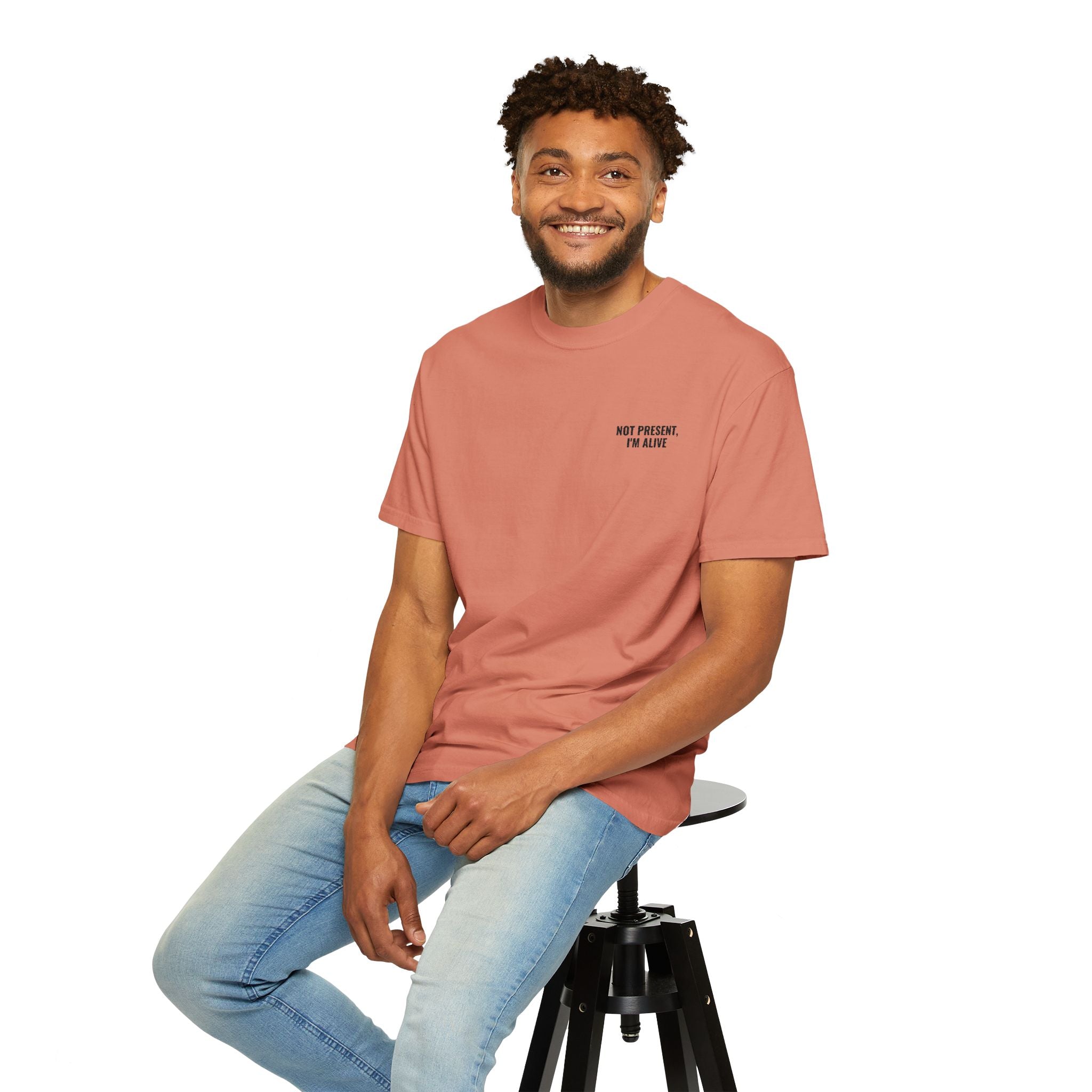 Man sitting on a stool wearing a pink t-shirt with a logo and light blue jeans on a white background