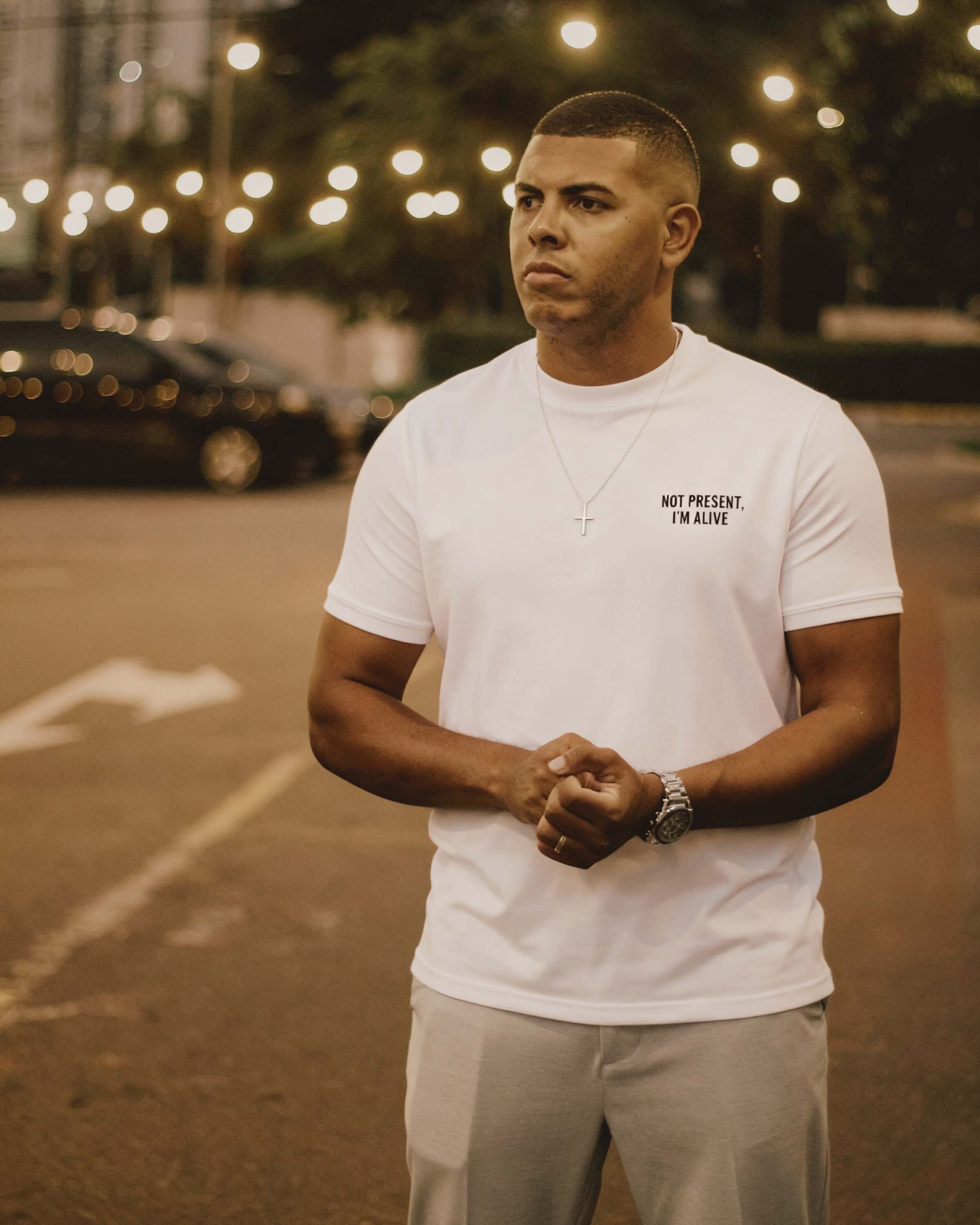 Man wearing a white t-shirt with IKIRU branding standing in an urban setting with lights and cars.