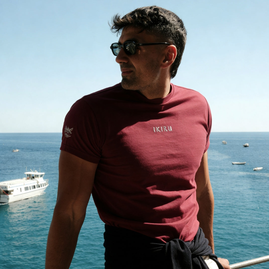 Man wearing a maroon t-shirt with 'IKIRU' logo by the sea