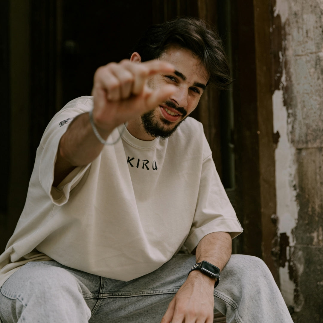 Man wearing a beige oversized t-shirt with the IKIRU logo, sitting outdoors.