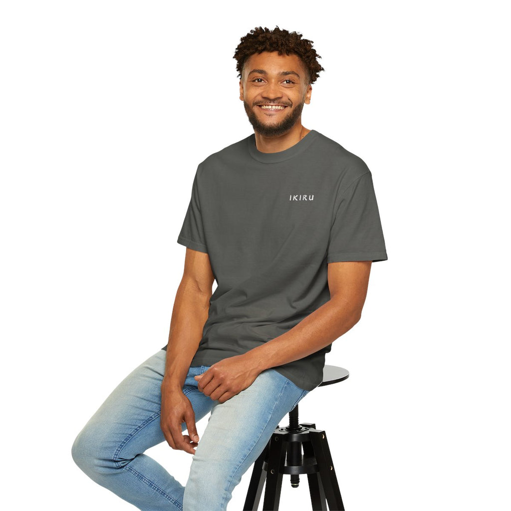 Man sitting on a stool wearing a gray t-shirt and light blue jeans against a white background